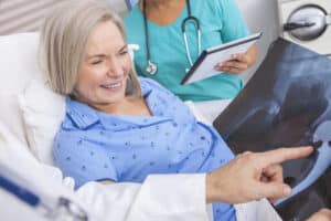 Woman in hospital bed happily recovering hip replacement as doctor shows her x-rays