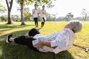 Elderly woman on ground holding her hip after a fall, with family running toward her