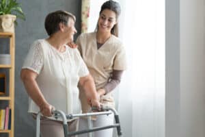 Medical professional helping older woman use walker after successful hip revision surgery.