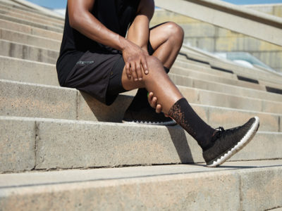 Cropped portrait of black male runner wearing black training outfit touching his leg in pain
